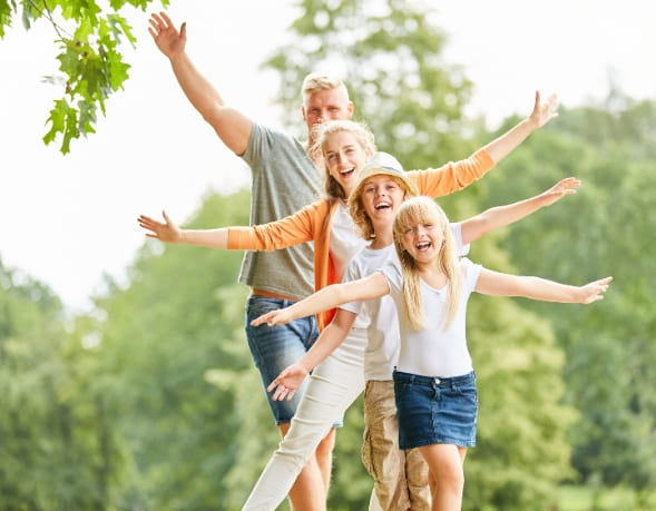 Familie balanciert auf einem Baum, die Kinder und die Eltern sind glücklich und lachen, weil sie durch die Reflexintegration eine leichteres Familienleben haben. Im Hintergrund sind Bäume zu erkennen.